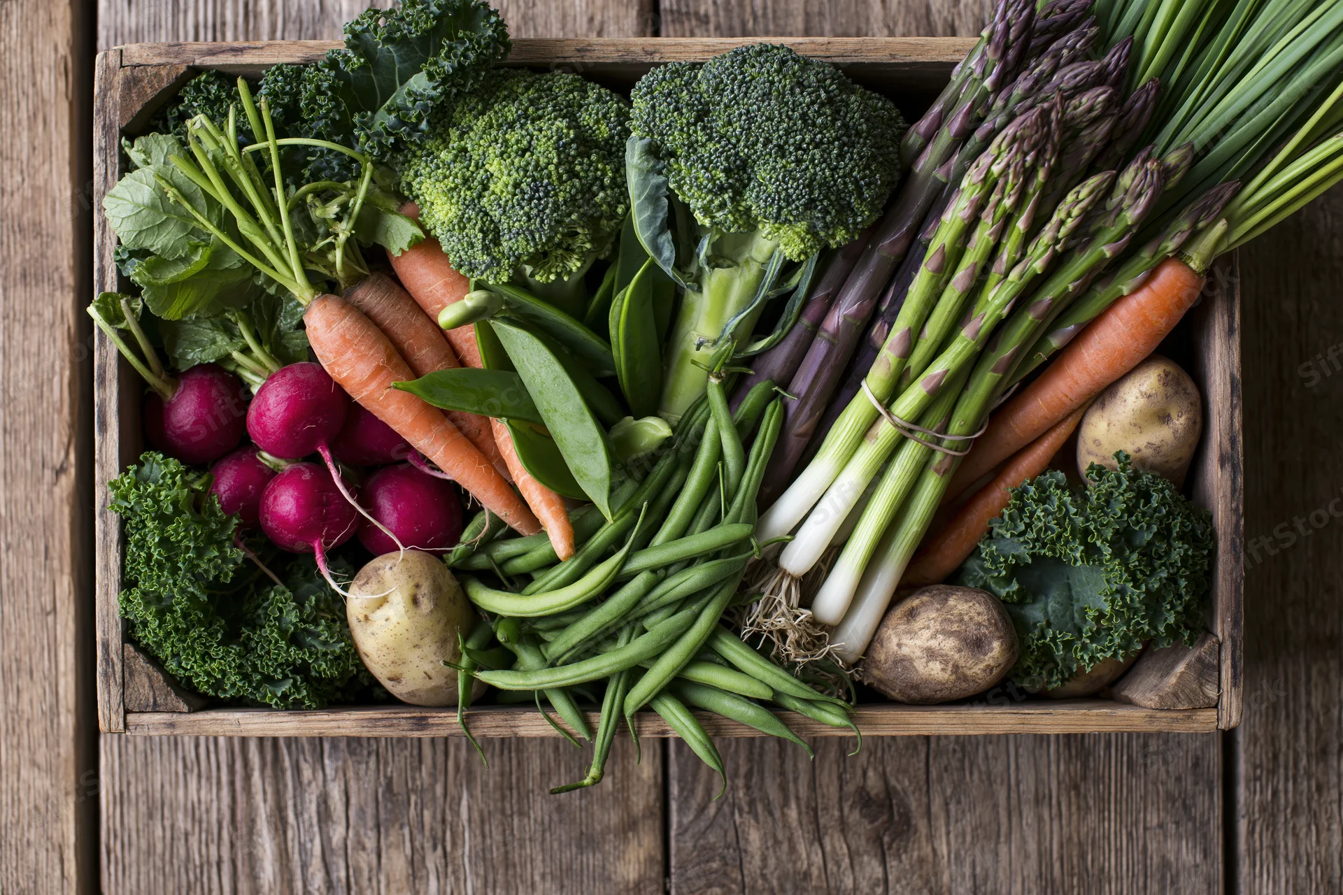 Overhead flat lay of a wooden crate filled with fresh vegetables on a rustic wooden surface