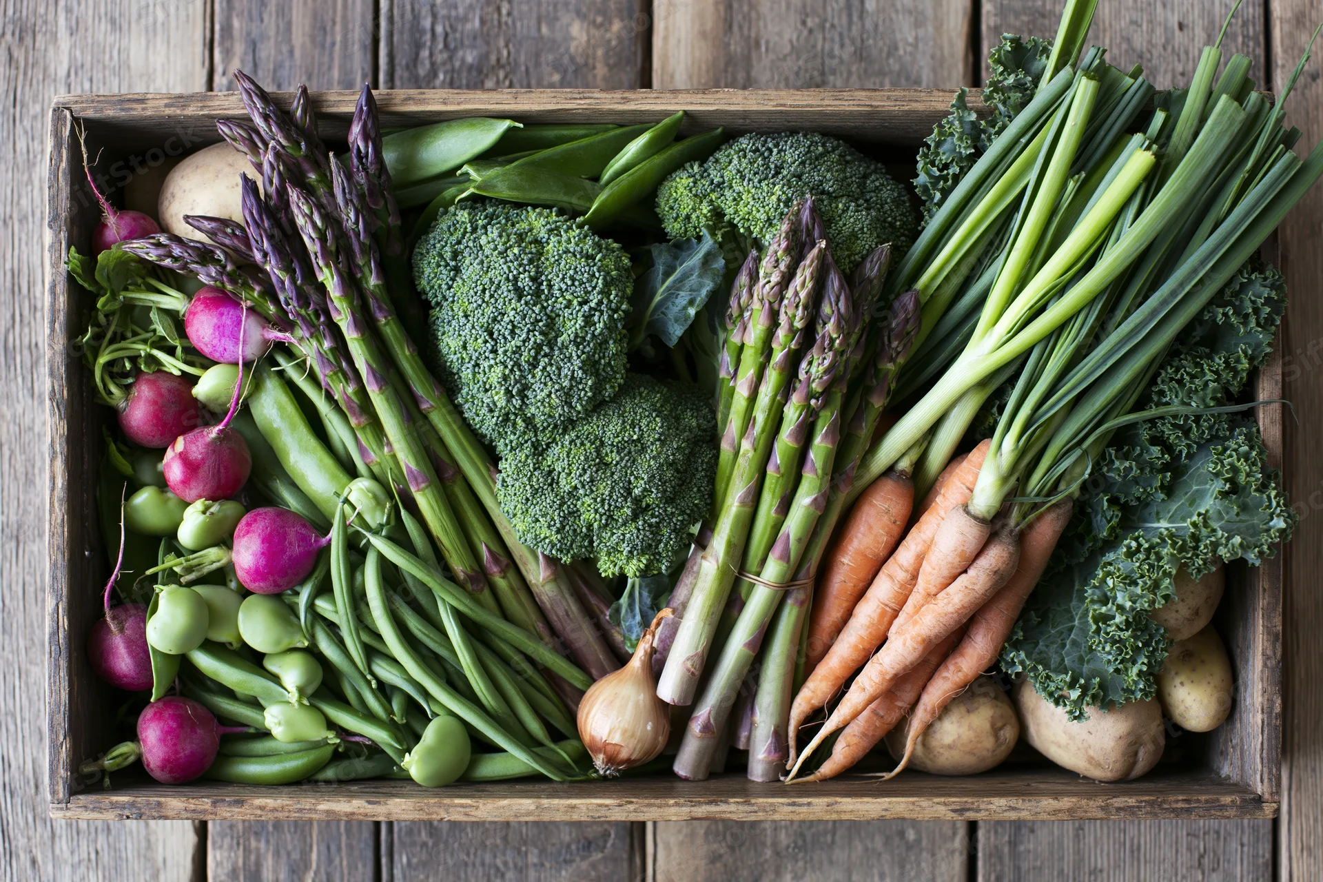 Overhead view of a wooden crate filled with fresh vegetables arranged in a flat lay on a rustic wooden surface