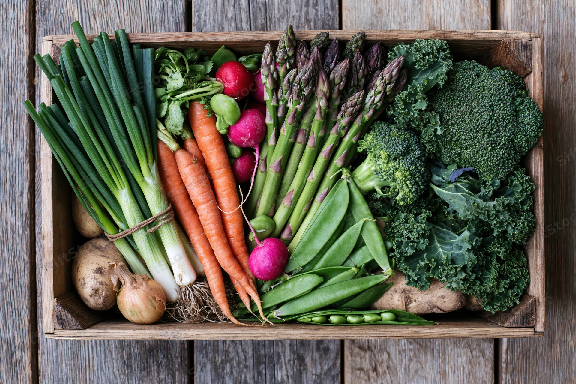 Wooden crate filled with fresh vegetables arranged in flat lay overhead view on rustic wood surface