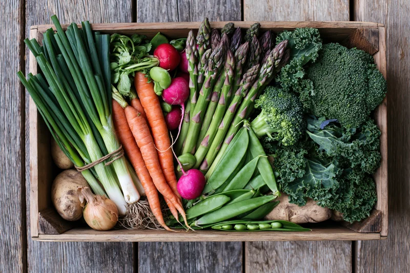 Wooden crate filled with fresh vegetables arranged in flat lay overhead view on rustic wood surface