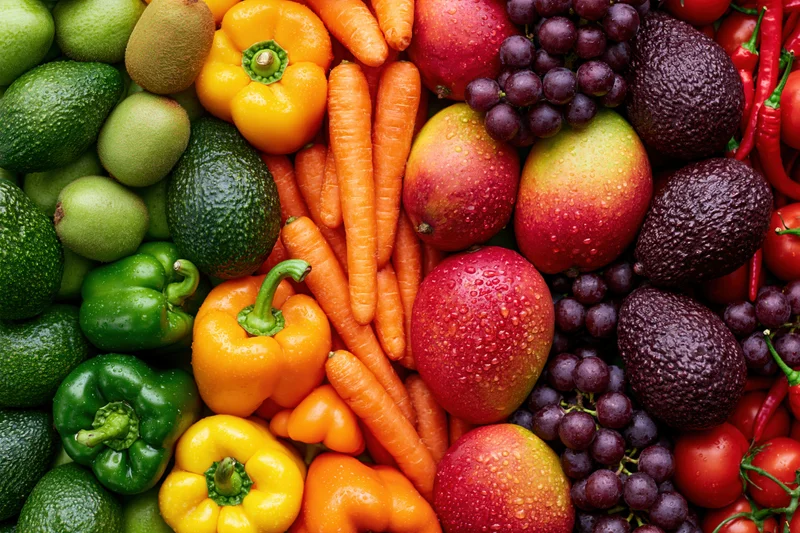 Overhead flat lay of densely packed fresh fruits and vegetables with water droplets on a flat surface