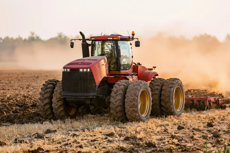 Red autonomous tractor plowing a field at sunset with led lights on and dust rising behind it