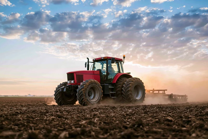 Red tractor pulling a wide disc harrow across a freshly tilled field at sunset