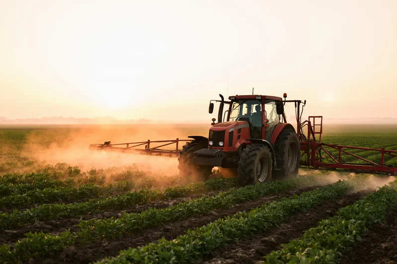 Red tractor pulling a boom sprayer across rows of low crops