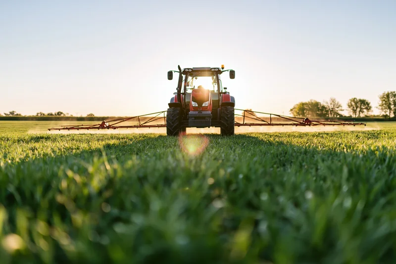 Red tractor pulling a wide sprayer across an agricultural field
