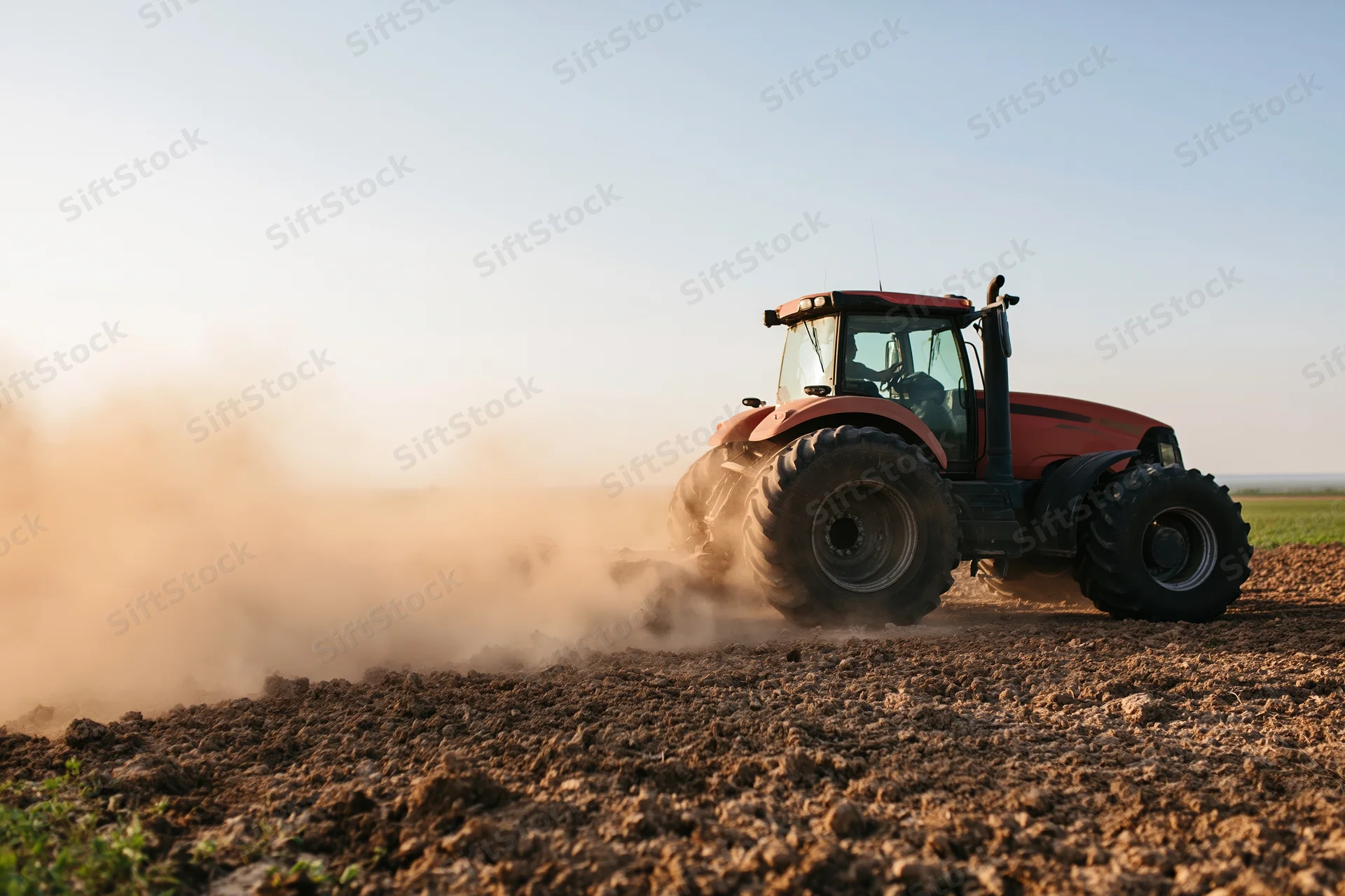 Red tractor tilling a dry field and kicking up a large dust cloud during golden hour