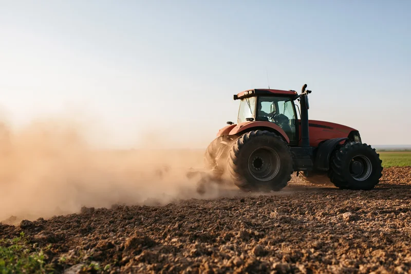 Red tractor tilling a dry field and kicking up a large dust cloud during golden hour