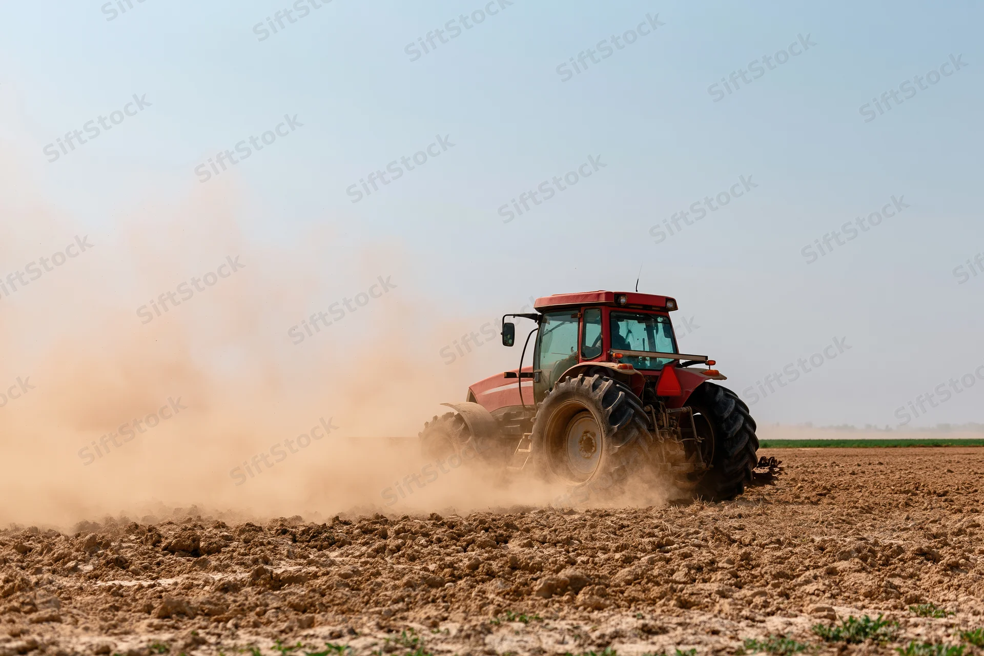 Red tractor tilling a dry field and kicking up a large dust cloud