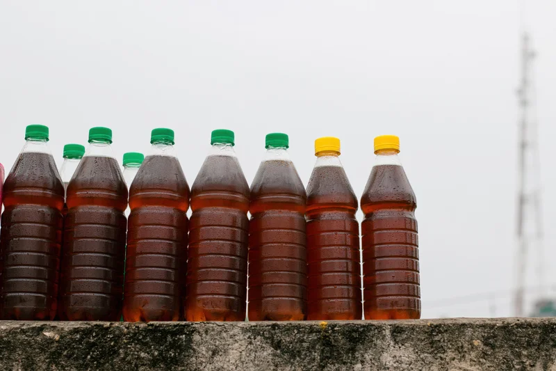 Row of reused plastic bottles filled with dark amber liquid arranged on concrete ledge outdoors