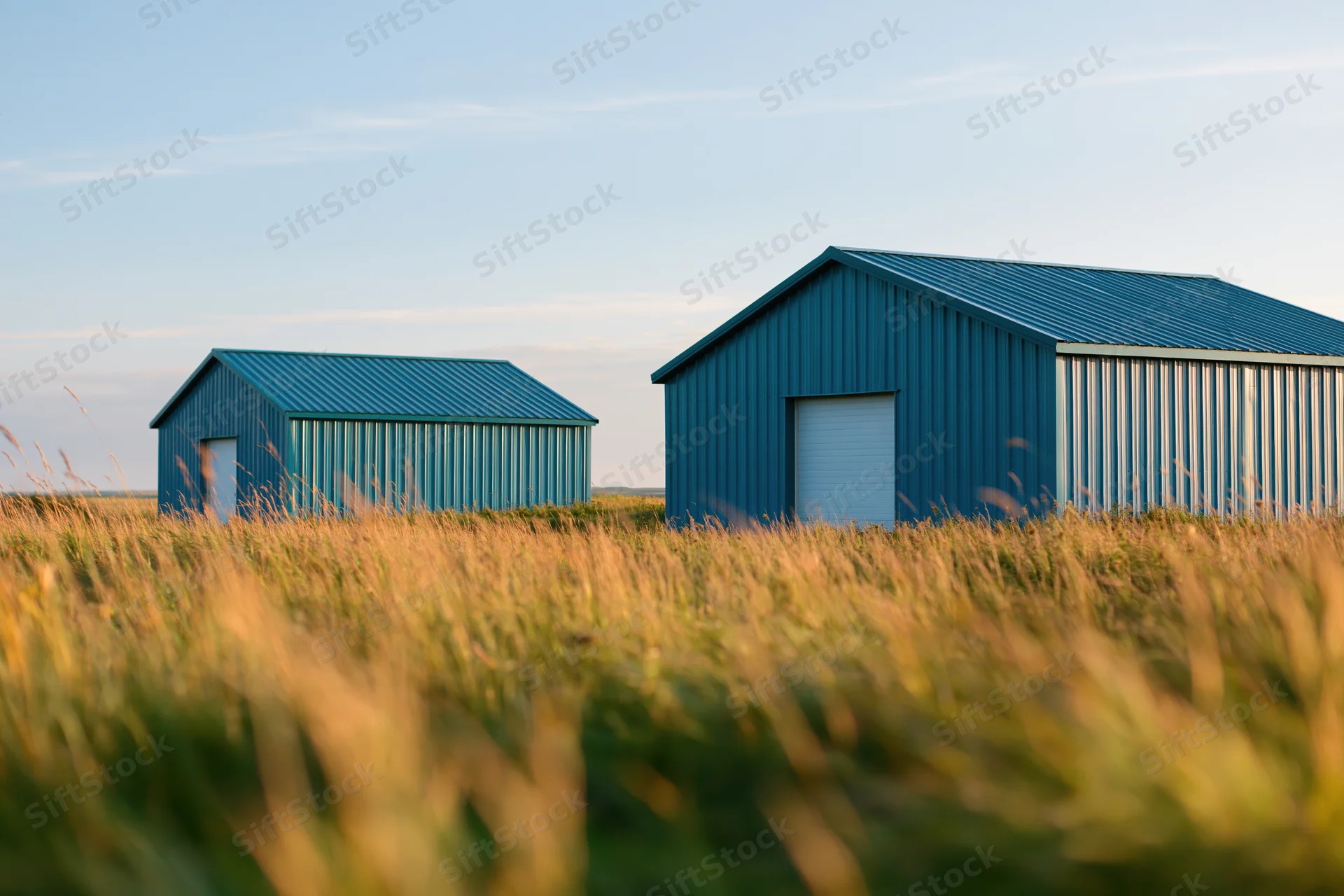 Two blue corrugated metal sheds standing in a grassy field under a clear sky