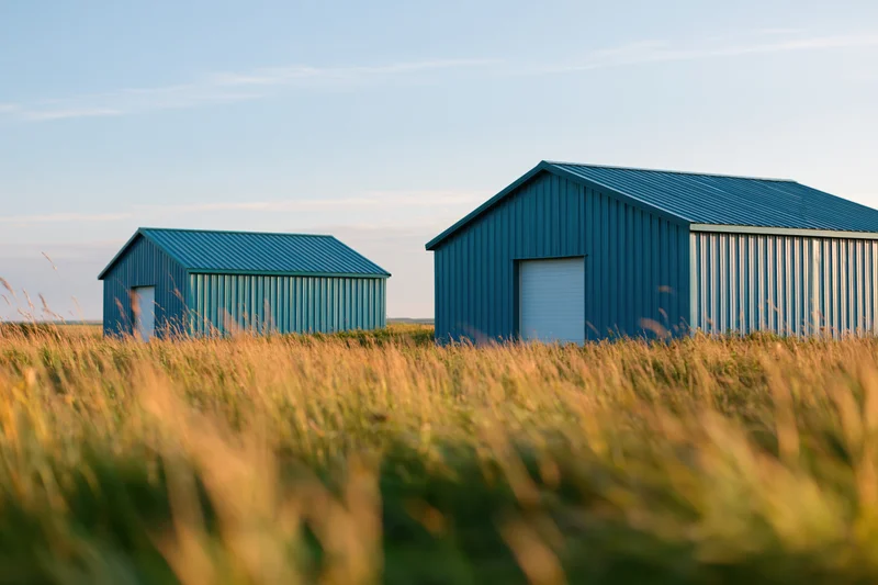 Two blue corrugated metal sheds standing in a grassy field under a clear sky