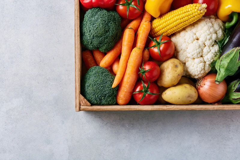Wooden crate filled with fresh vegetables arranged on a light gray surface