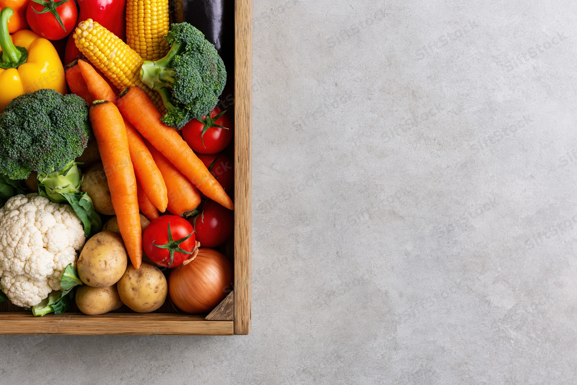 Wooden crate filled with fresh vegetables arranged on a gray surface with copyspace