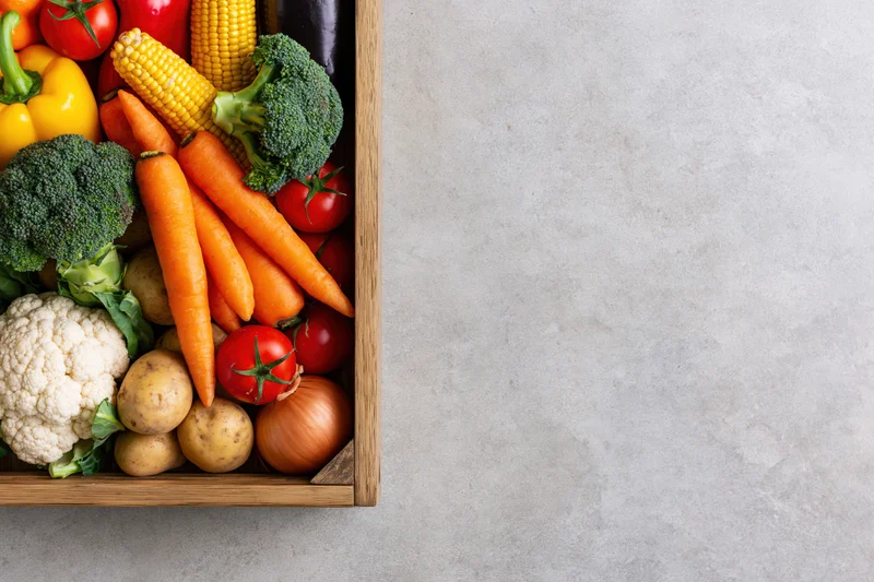 Wooden crate filled with fresh vegetables arranged on a gray surface with copyspace