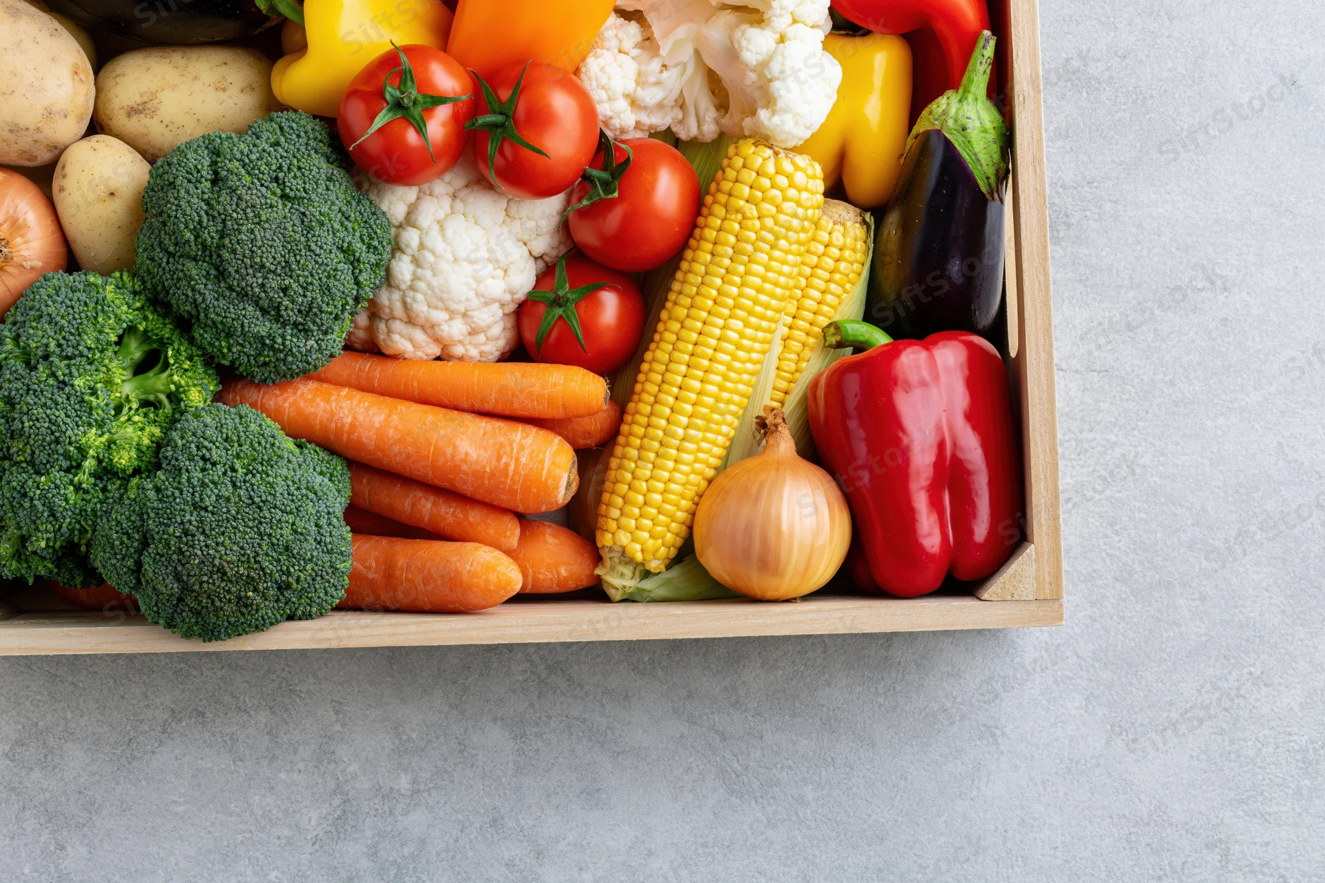 Wooden crate filled with assorted fresh vegetables arranged on a gray surface