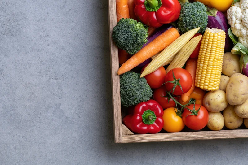 Wooden crate filled with fresh mixed vegetables arranged on gray surface with copyspace