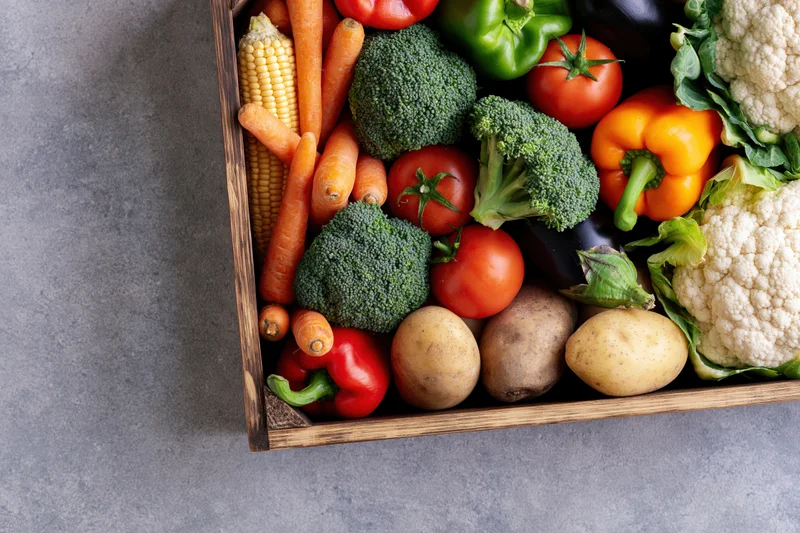 Wooden crate filled with fresh mixed vegetables arranged on gray surface