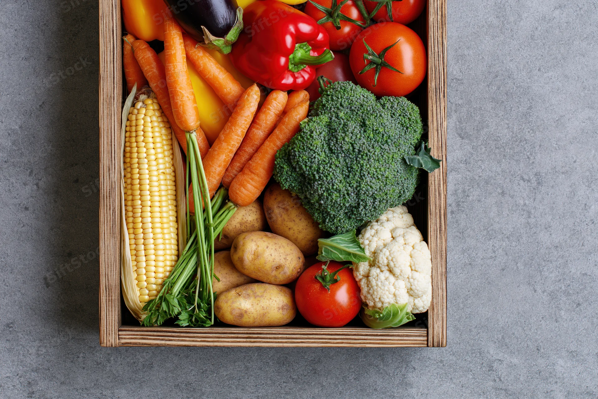 Wooden crate filled with fresh mixed vegetables arranged on gray surface