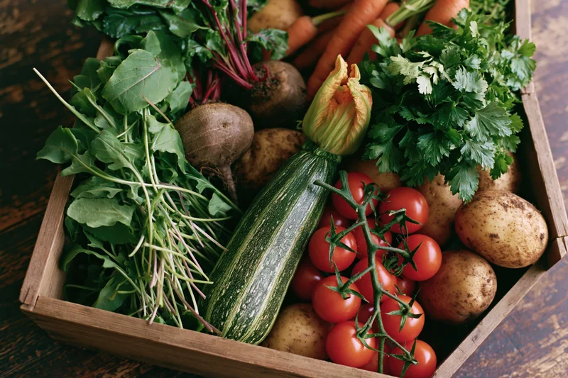Wooden crate filled with freshly harvested vegetables arranged on a rustic surface