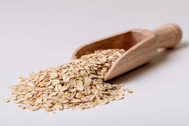 Wooden scoop resting on a small pile of dry rolled oats with some spilled onto the surface
