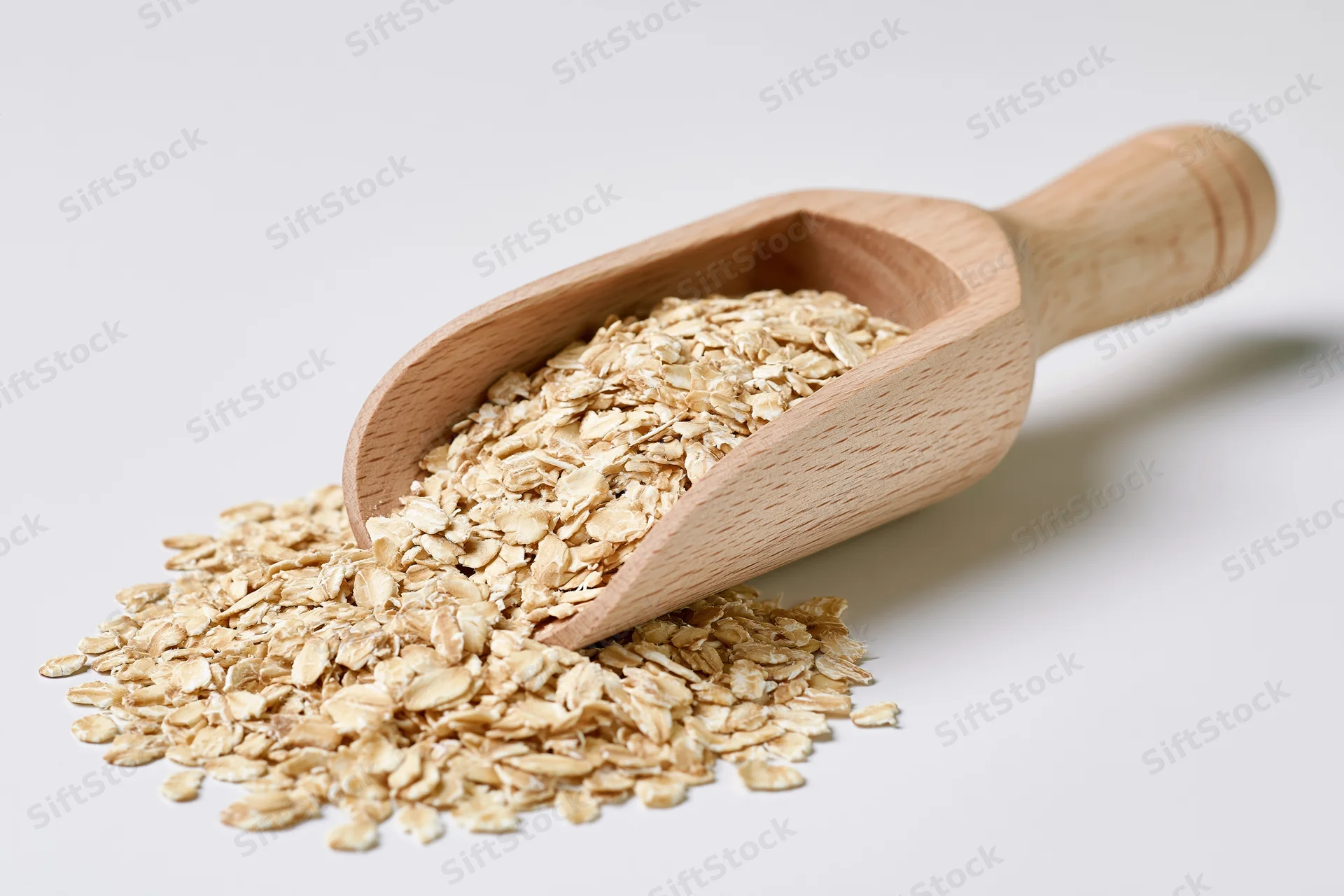 Wooden scoop resting on a small pile of dry rolled oats spilling onto a white surface