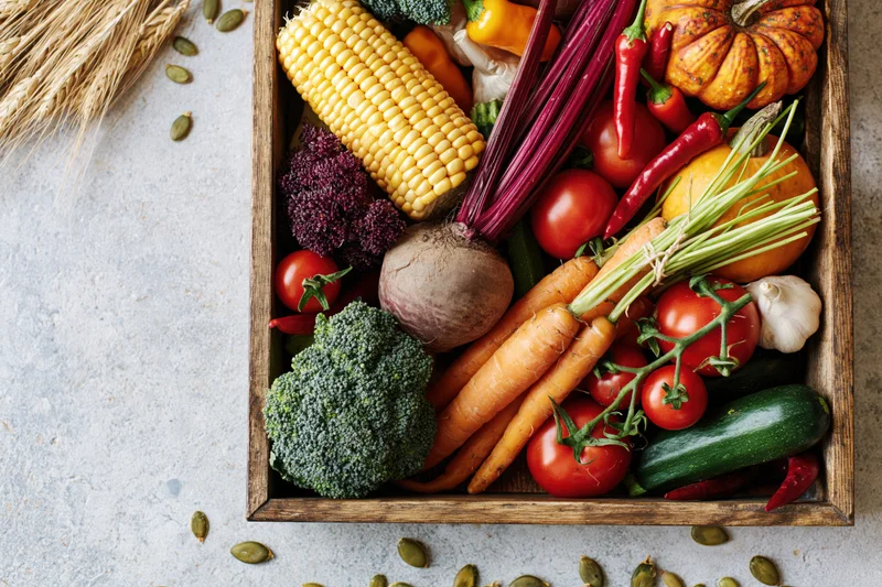 Wooden tray filled with fresh autumn harvest vegetables arranged on a light surface