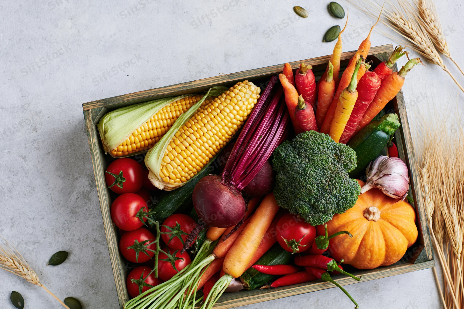 Wooden tray filled with fresh autumn harvest vegetables arranged on a light surface