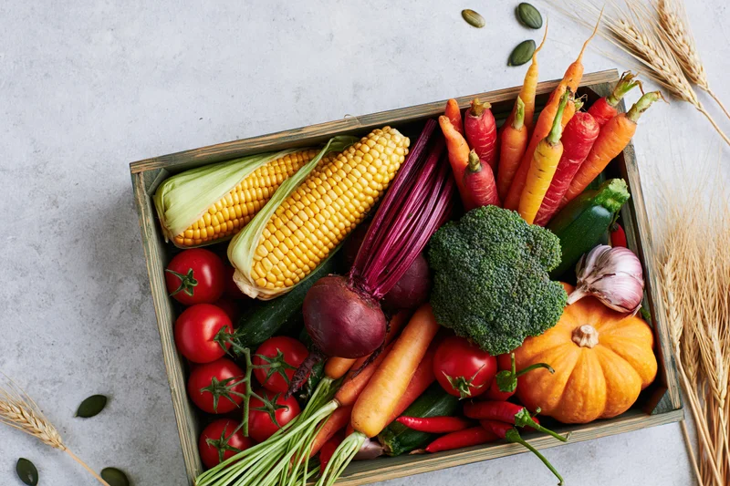 Wooden tray filled with fresh autumn harvest vegetables arranged on a light surface