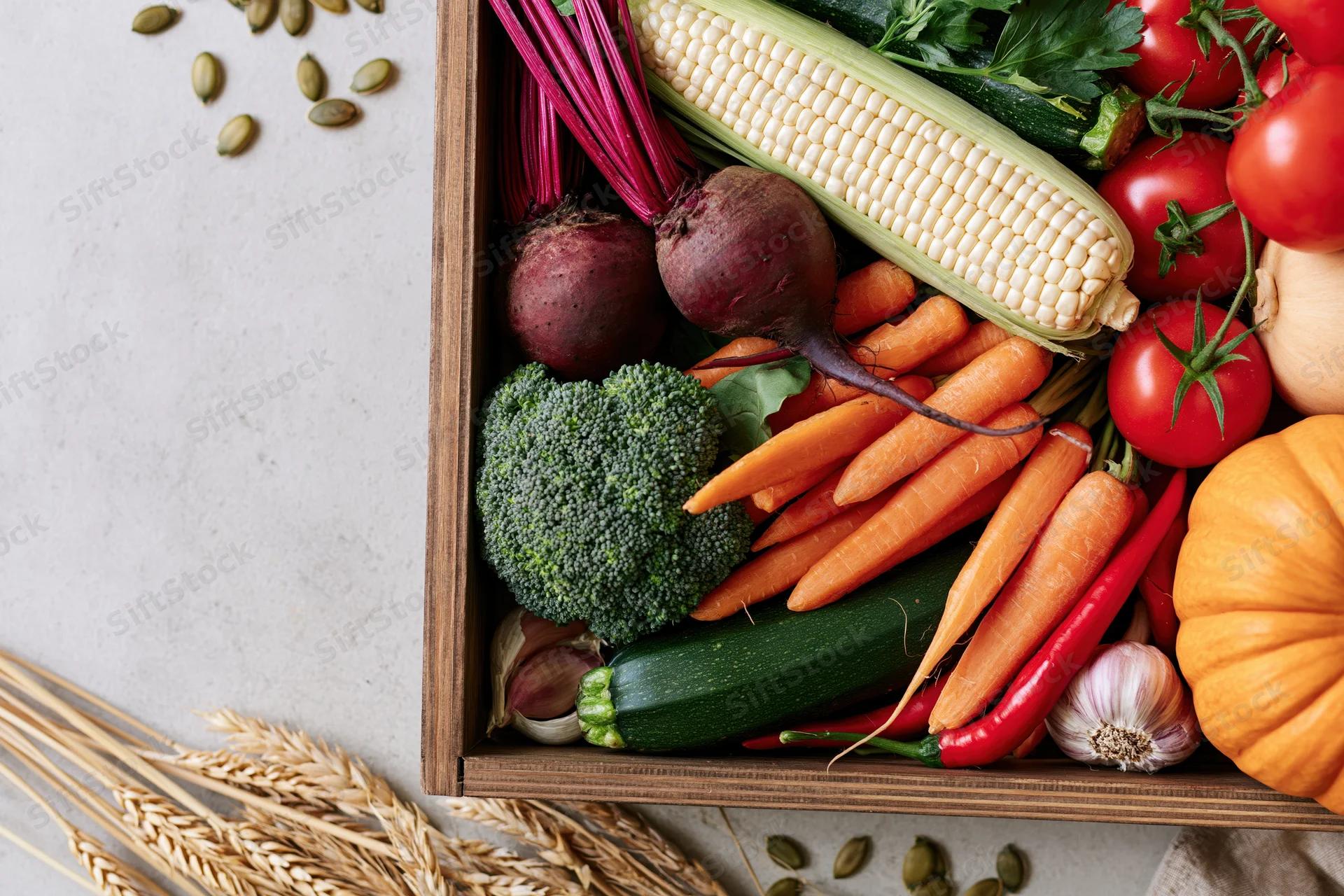 Wooden tray filled with fresh autumn harvest vegetables arranged on a light surface with scattered wheat and pumpkin seeds