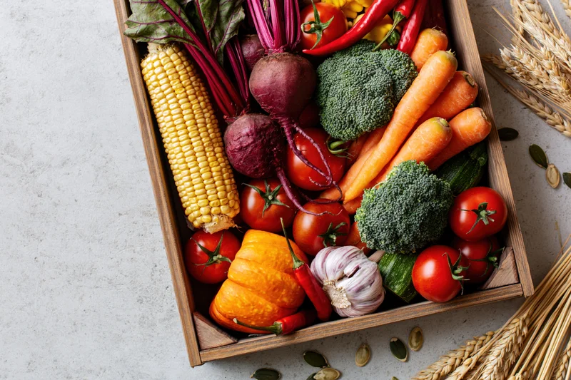 Wooden tray filled with fresh autumn harvest vegetables arranged on a light surface