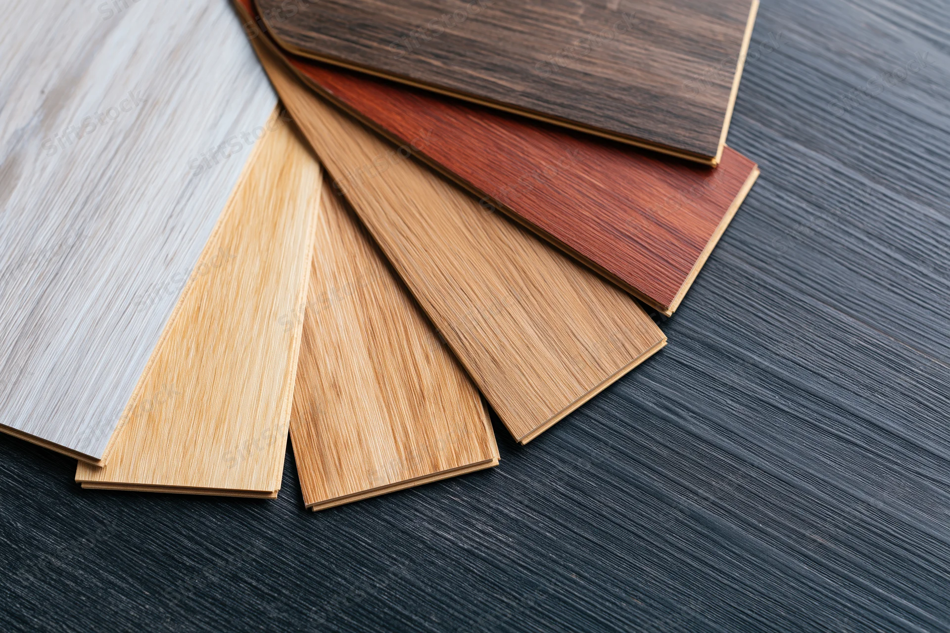 Fan arrangement of wood laminate flooring samples on dark textured surface