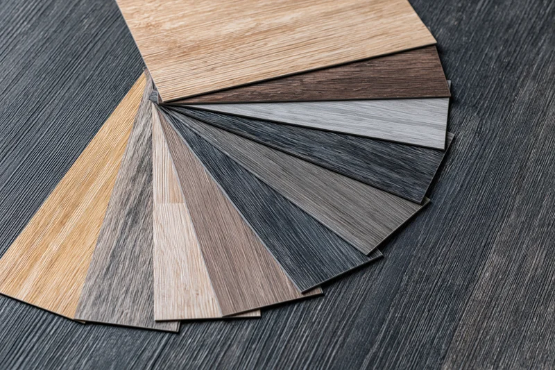 Fan of wood-grain vinyl flooring samples arranged on dark textured surface