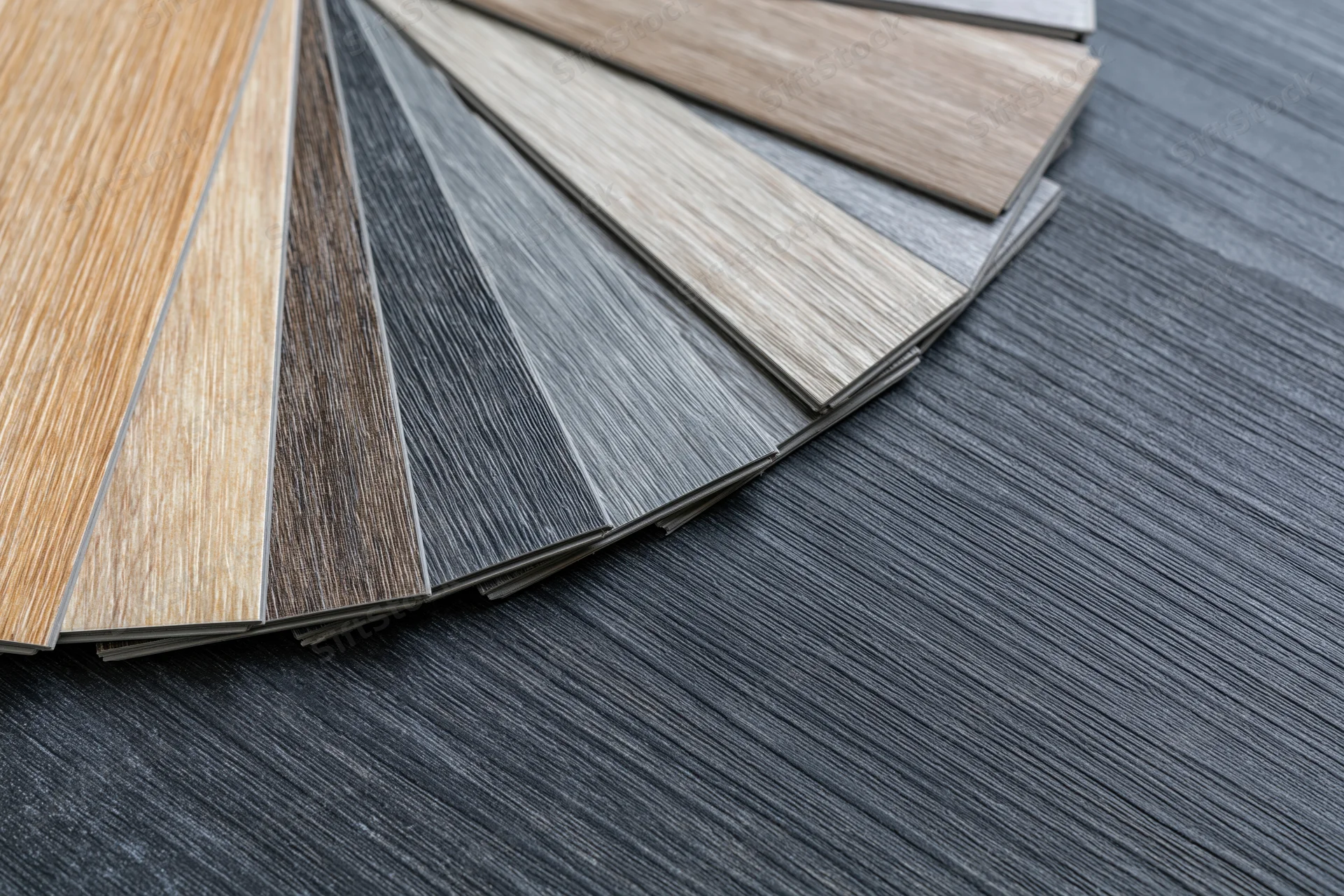Fan of wood-grain vinyl flooring samples arranged on dark textured floor