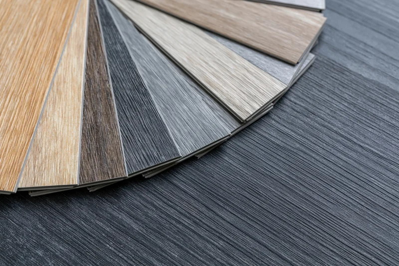 Fan of wood-grain vinyl flooring samples arranged on dark textured floor