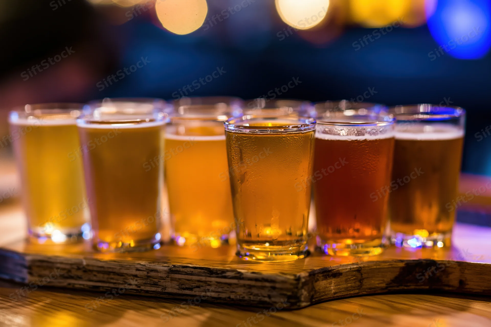 Flight of craft beer glasses arranged in two rows on a wooden tray in a dimly lit bar setting