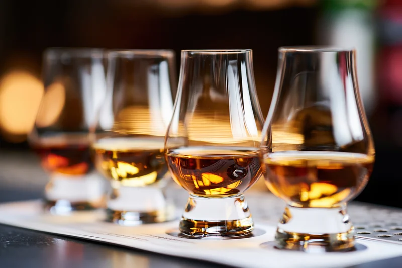 Five glencairn glasses filled with amber whisky arranged in a row on a tasting mat