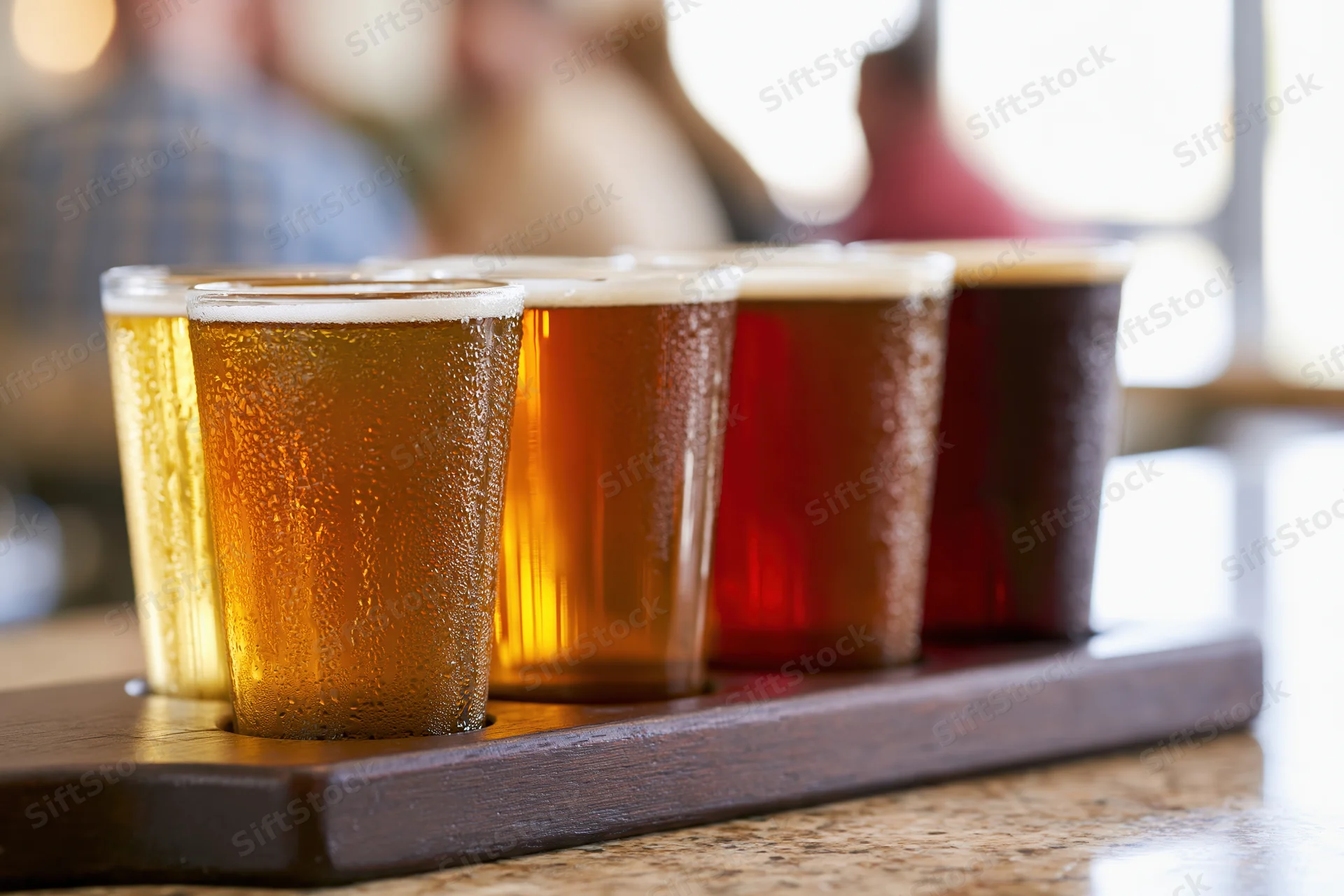 Five small craft beer tasting glasses arranged in a wooden tray on a countertop