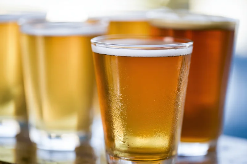 A flight of four craft beer tasting glasses lined up in a row with condensation and foam on a wooden surface