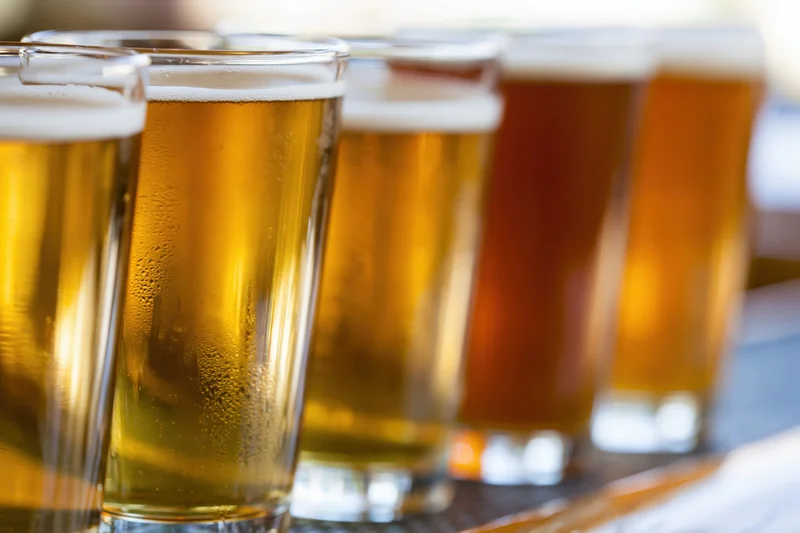 A row of craft beer tasting glasses filled with different colored beers arranged on a tray