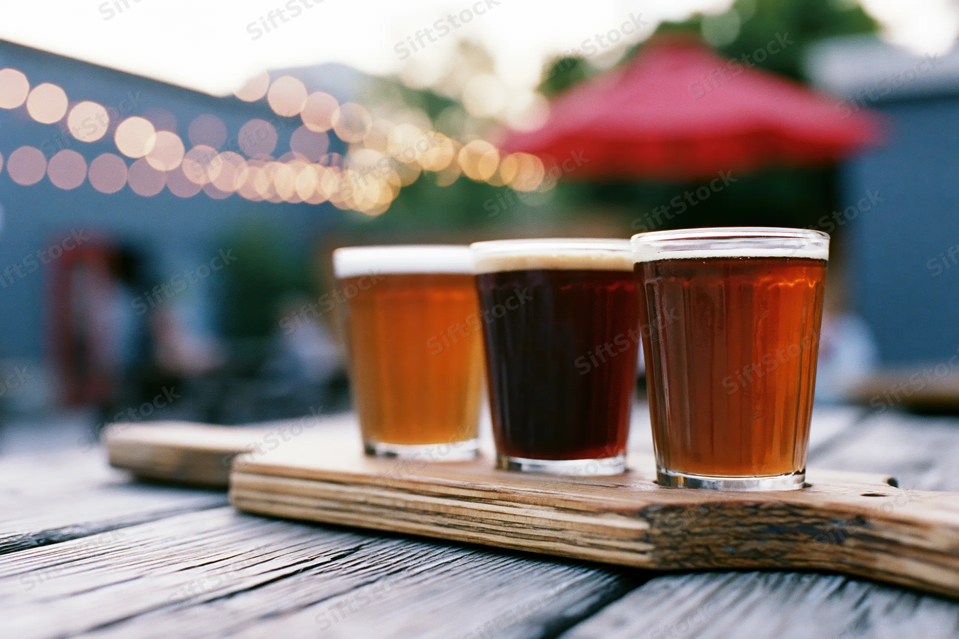 Craft beer flight in small glasses arranged on wooden tray on outdoor patio table at evening