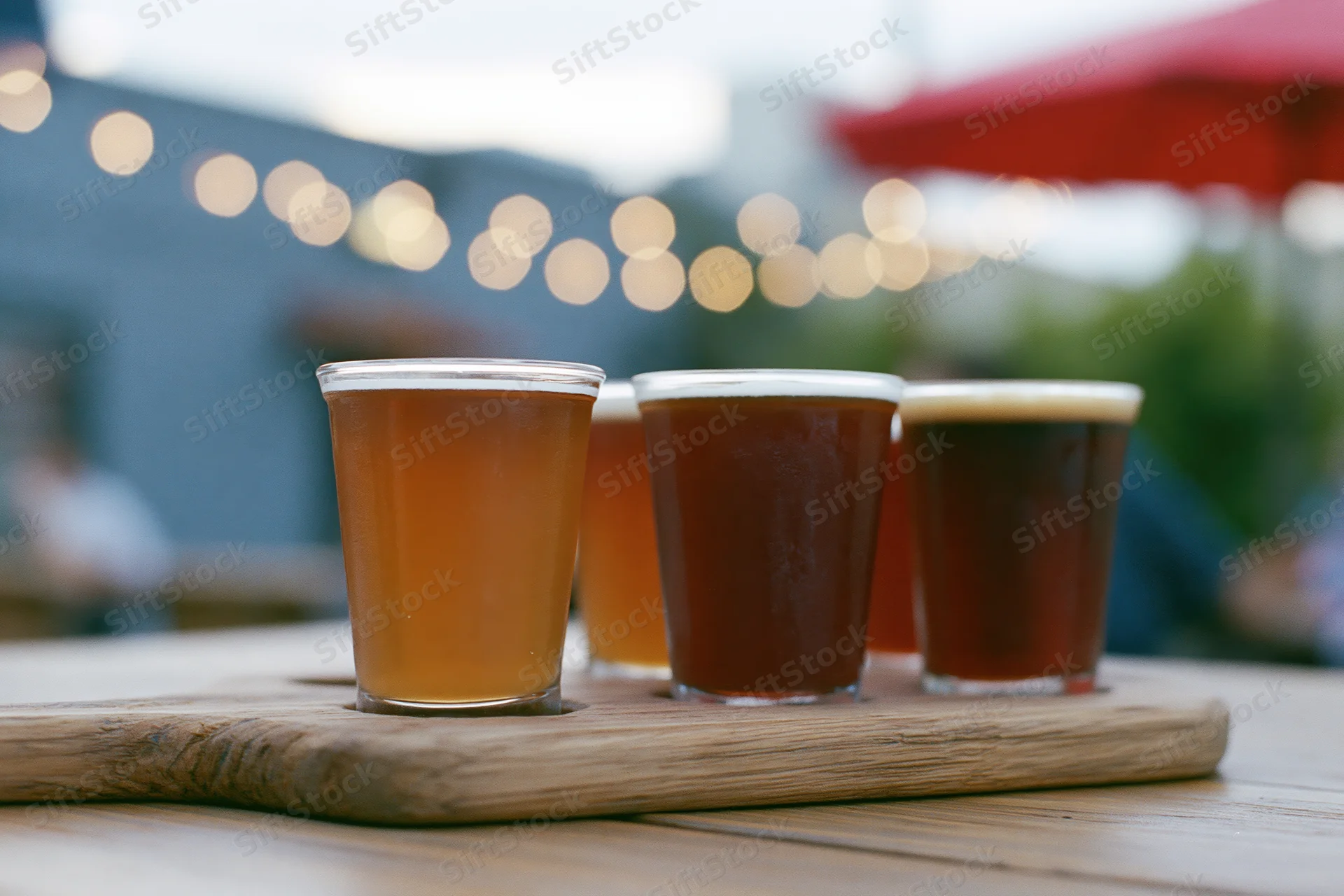 Four craft beers in small glasses arranged on a wooden tray on an outdoor patio table