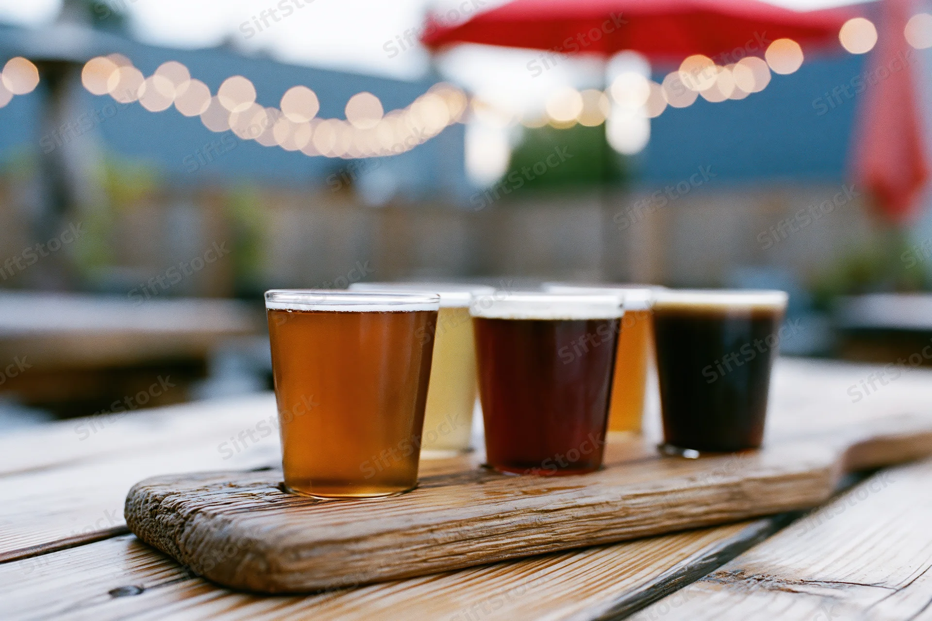 Four craft beers in small glasses arranged on a wooden tray on an outdoor patio table at twilight