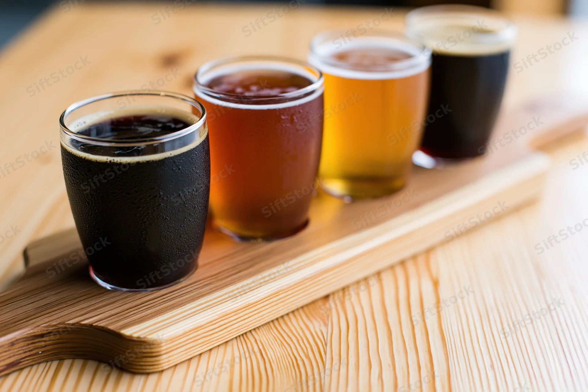 Four craft beers in small tasting glasses arranged on a wooden tray