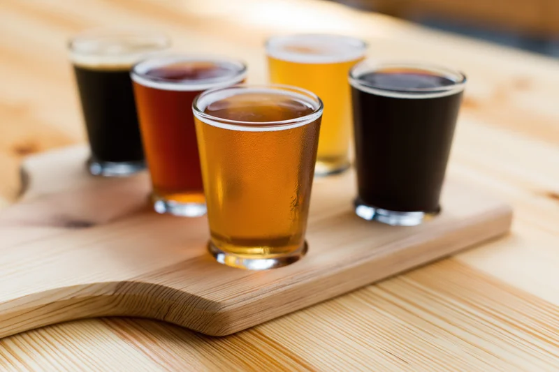 Craft beer flight in small tasting glasses arranged on a wooden tray