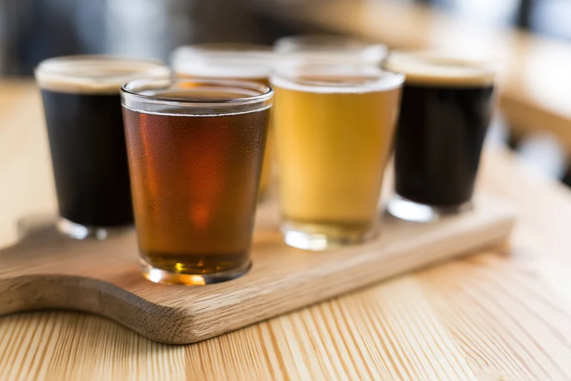 Flight of craft beers in small tasting glasses arranged on a wooden tray on a table