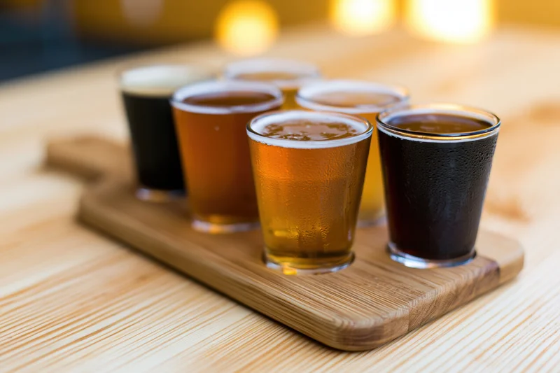 Craft beer flight in small tasting glasses arranged on wooden tray on table