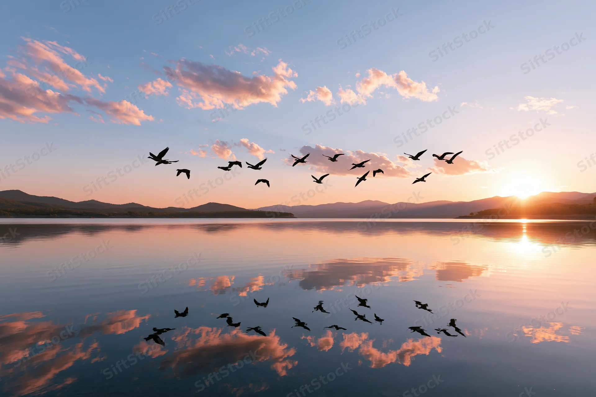 Flock of birds in flight over calm lake at sunset with mountain horizon and sky reflection