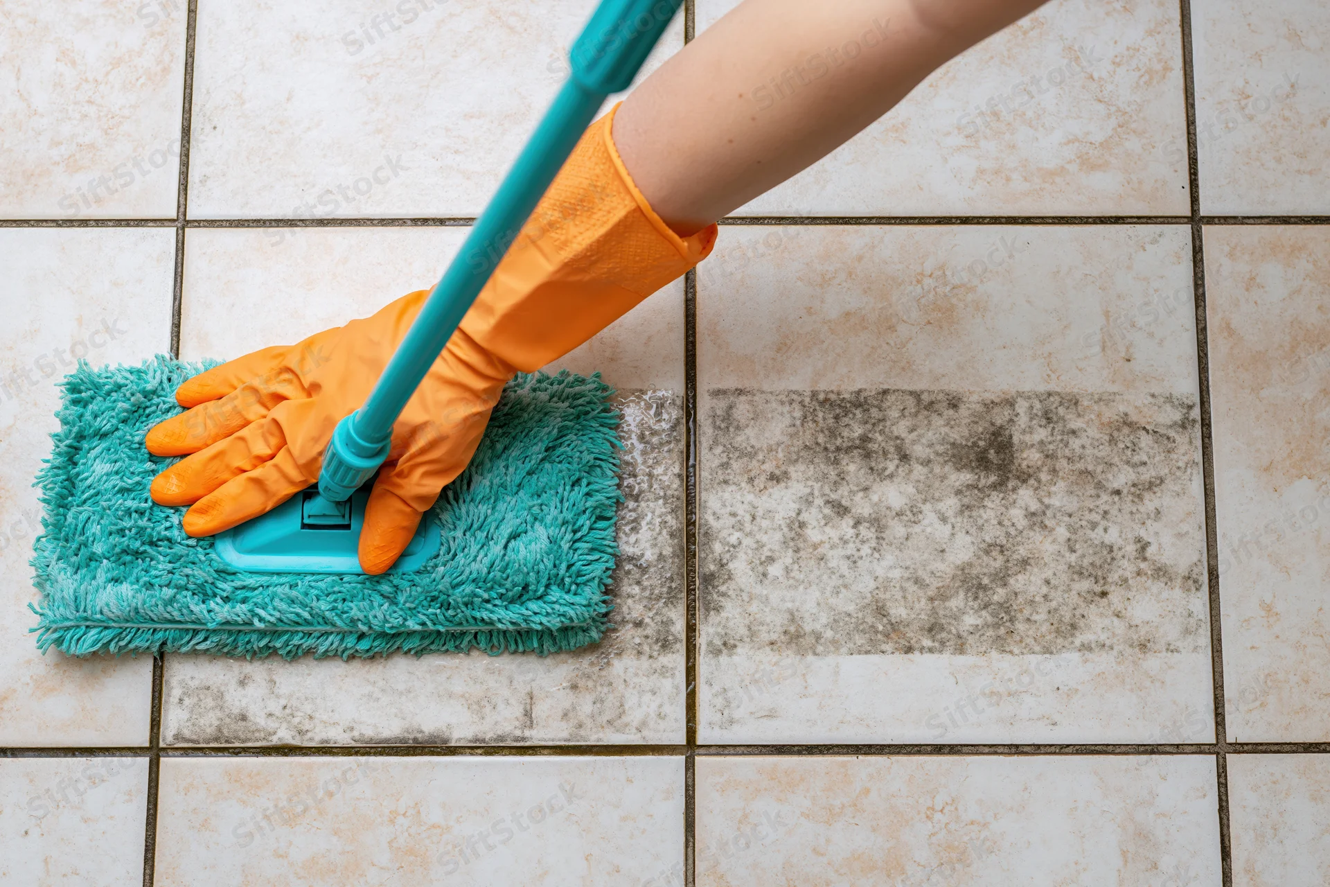 Gloved hand pushing a turquoise flat mop across dirty ceramic tile floor