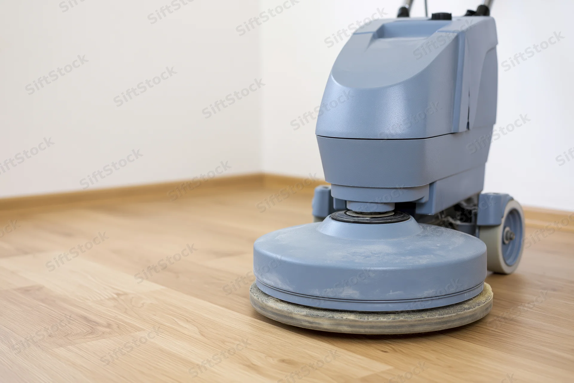 Gray-blue commercial floor polishing machine resting on light hardwood flooring in an interior room corner
