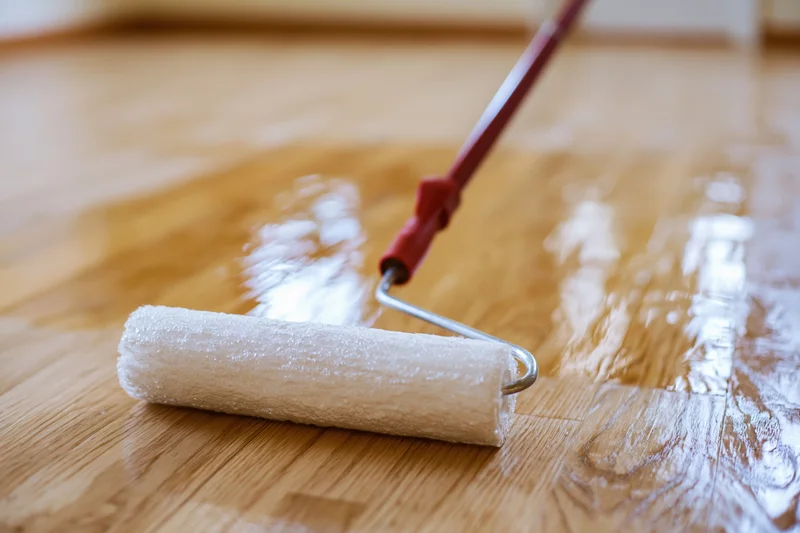 Paint roller applying clear varnish to wooden floor